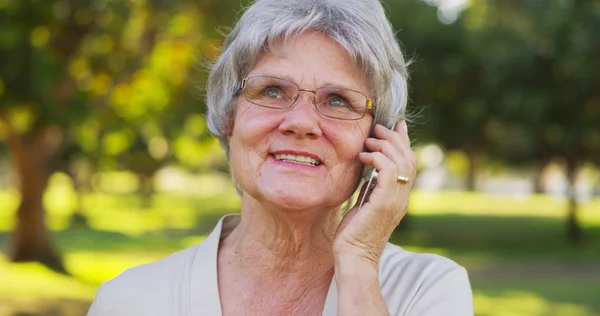 Äldre kvinna talar på smartphone på park — Stockfoto