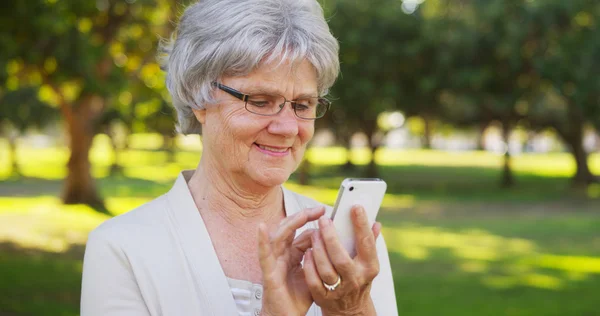 Starší žena textilie na smartphone v parku — Stock fotografie