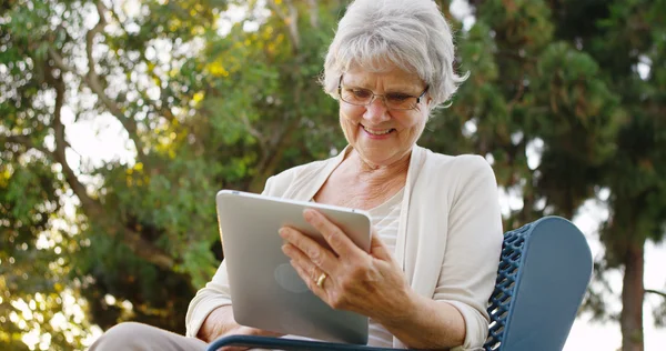 年配の女性が喜んで公園でタブレット上の web をサーフィン — ストック写真