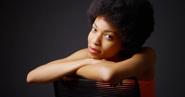 Sorrindo mulher negra sentada com os braços na parte de trás da cadeira — Fotografia de Stock