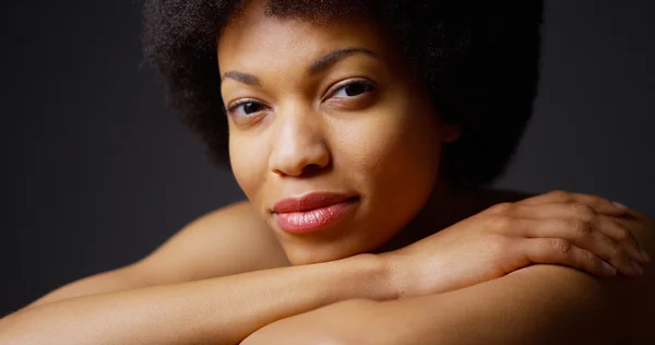 Femme noire assise avec les bras croisés souriant sur fond gris — Photo