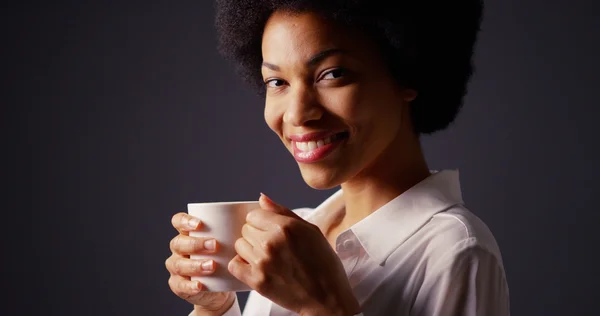Mulher negra com afro no estúdio bebendo café quente e sorrindo — Fotografia de Stock