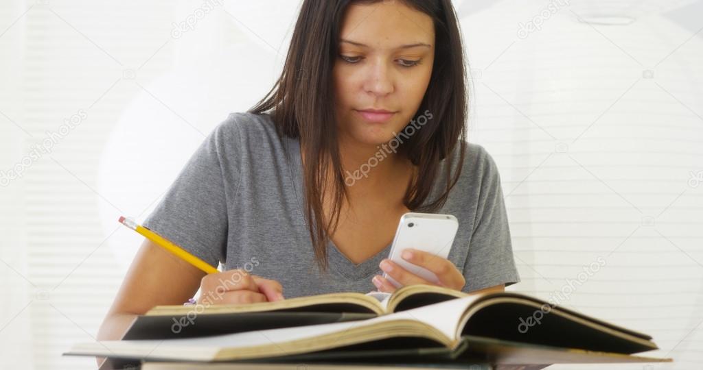 Hispanic woman studying and using smartphone on desk