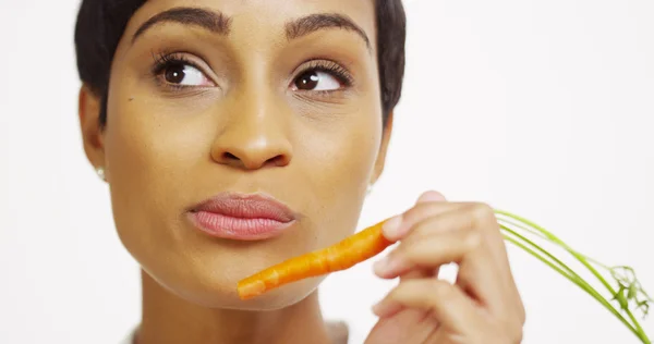 Close up of African woman eating carrot and smiling — Stock Photo, Image