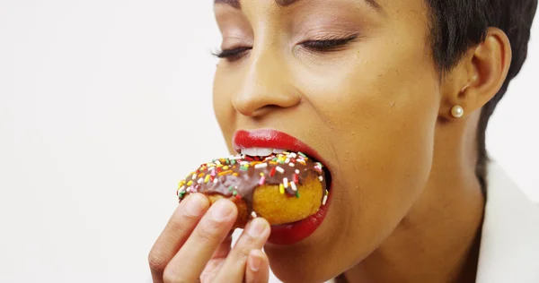Черная женщина ест шоколадный пончик с брызгами и улыбается — стоковое фото