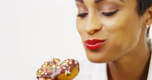 Black woman eating chocolate donut with sprinkles and smiling