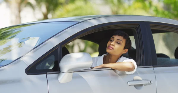 Черная женщина в машине смотрит вокруг и проверяет волосы в зеркале — стоковое фото