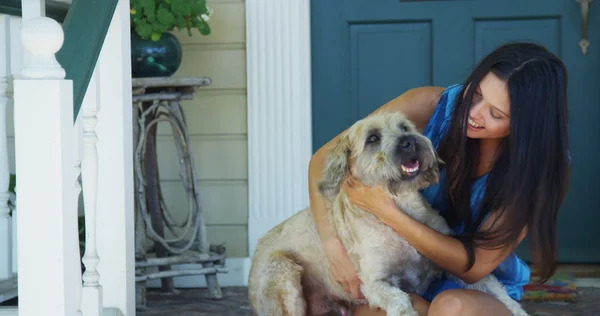 Hispanic woman sitting on porch scratching dog — Stock Photo, Image