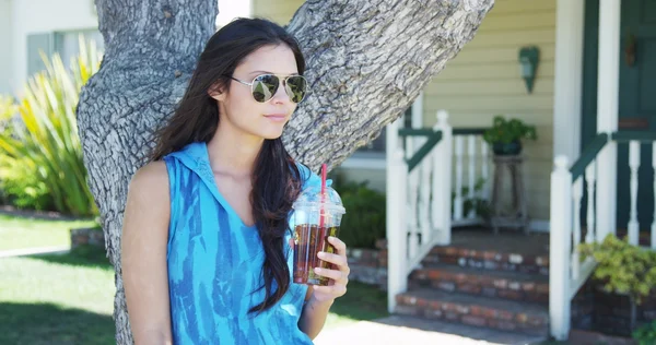 Mujer de raza mixta parada junto al árbol bebiendo té helado —  Fotos de Stock