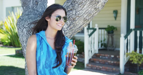 Mujer de raza mixta parada junto al árbol bebiendo té helado — Foto de Stock