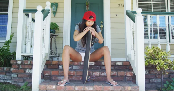 Donna ispanica seduta sul portico con skateboard — Foto Stock