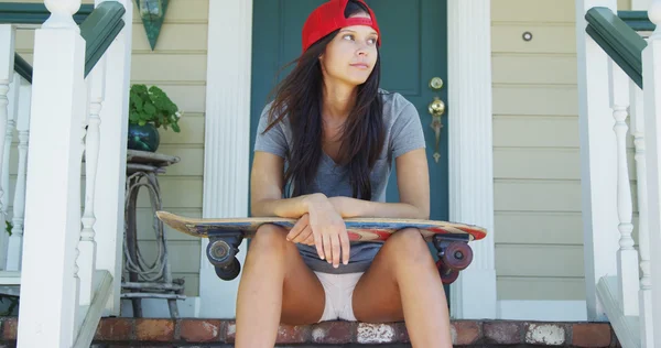 Young woman sitting on porch with skateboard — Stock Photo, Image