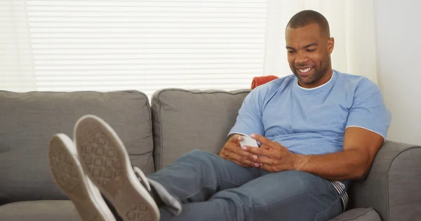 Black man sitting on couch texting — Stock Photo, Image