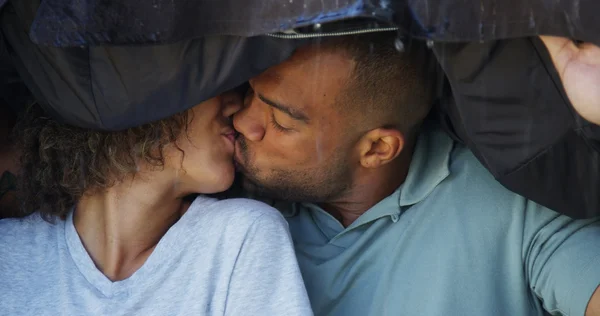 Casal preto de pé sob o casaco tentando não ficar molhado — Fotografia de Stock