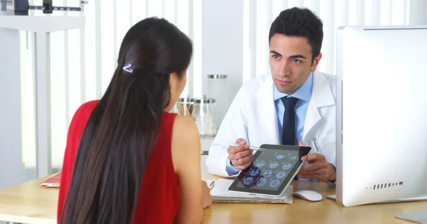 Médico hispano revisando radiografías cerebrales con paciente en el escritorio —  Fotos de Stock