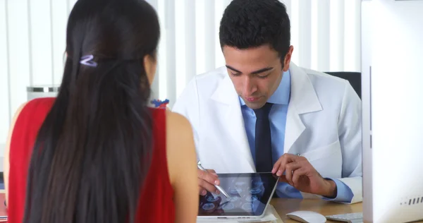 Spanischer Arzt überprüft Röntgenbilder des Gehirns auf Tablet mit Patient am Schreibtisch — Stockfoto