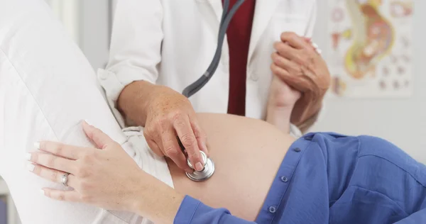 Médico sênior ouvindo o estômago da mulher grávida — Fotografia de Stock