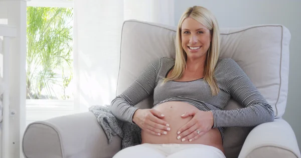 Lächelnde Schwangere reibt sich Bauch im Kinderzimmer — Stockfoto