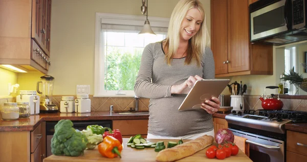 Piękna kobieta w ciąży za pomocą tabletu w kuchni — Zdjęcie stockowe