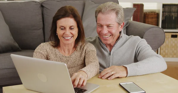 Feliz pareja de ancianos utilizando el ordenador portátil en la mesa de café —  Fotos de Stock