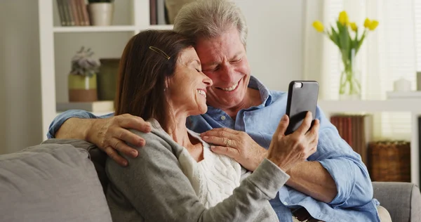 Lyckliga äldre par med smartphone på soffan — Stockfoto