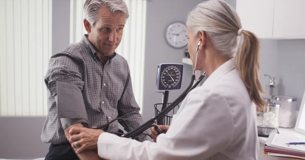 Médico profesional midiendo la presión arterial del hombre mayor — Foto de Stock