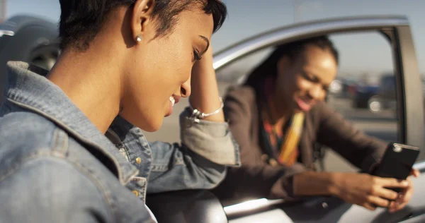 Duas mulheres negras amigos mensagens de texto no telefone celular e inclinando-se agains — Fotografia de Stock