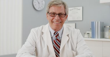 Kıdemli doktor kameraya gülümseyen masada oturan