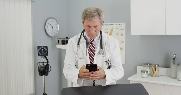 Médico maduro usando smartphone no escritório — Fotografia de Stock