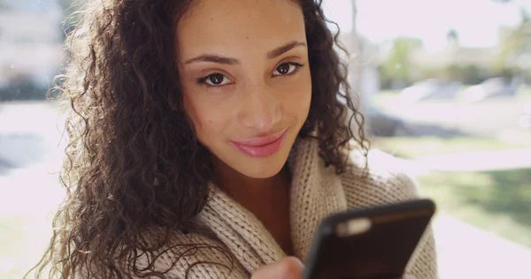 Attraktiv ung brunett på en mobiltelefon som ler mot kameran — Stockfoto