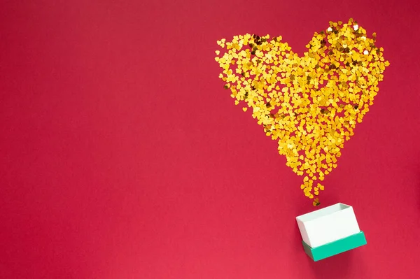 Kırmızı arka planda hediye kutusu olan kalp şeklinde altın parıltılar. Sevgililer Günü, Kadınlar Günü. Tatil günü. Düz Yatay