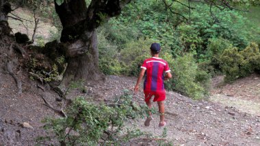 Köyün dağlarında koşan futbol üniformalı genç bir çocuk.
