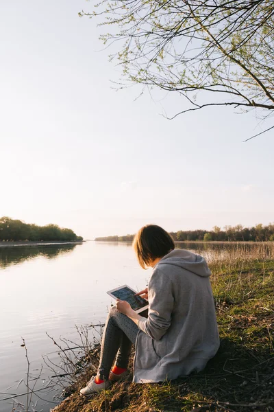 Девушка работает с планшетом на реке — стоковое фото