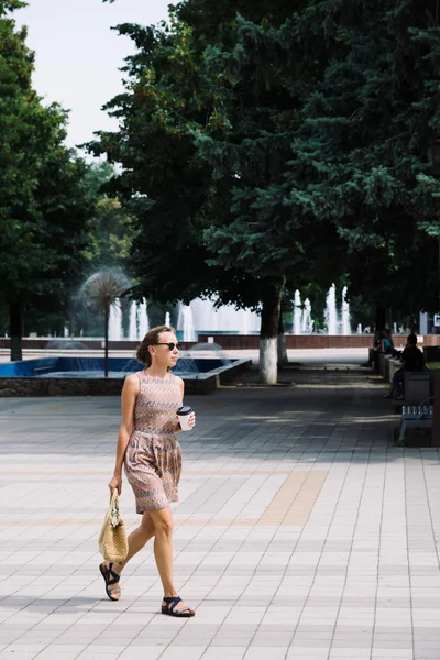 Young brunette woman with coffee cup walking in city — Stock Photo, Image