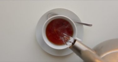 Çaydanlıktan gelen çay yavaşça porselen bardağa dökülüyor.