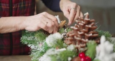 Çiçekçi kırmızı böğürtlenli, köknar dallı ve kozalaklı Noel sepeti yapar.