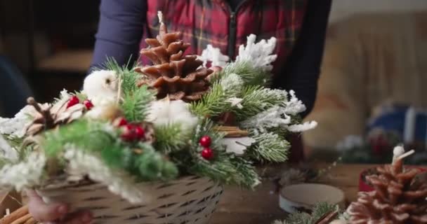Флорист делает Рождественскую корзину с красными ягодами, еловыми ветвями и хвойными конусами — стоковое видео