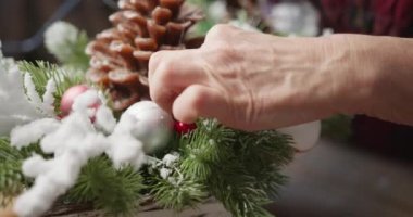 Çiçekçi kırmızı böğürtlenli, köknar dallı ve kozalaklı Noel sepeti yapar.