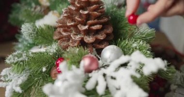 Çiçekçi kırmızı böğürtlenli, köknar dallı ve kozalaklı Noel sepeti yapar.