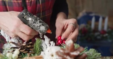 Çiçekçi kırmızı böğürtlenli, köknar dallı ve kozalaklı Noel sepeti yapar.