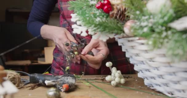 Флорист робить різдвяний кошик з червоними ягодами, ялиновими гілками та хвойними шишками — стокове відео
