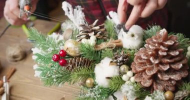 Çiçekçi kırmızı böğürtlenli, köknar dallı ve kozalaklı Noel sepeti yapar.