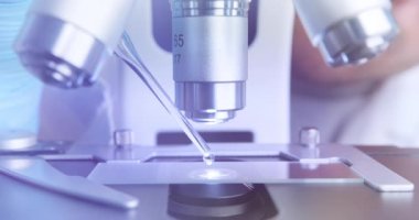Laboratuvar asistanı mikroskop altında detaylı inceleme için çözeltiyi damlatır.