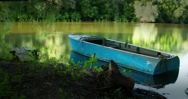 Antiguo barco azul atado con una cuerda al muelle de madera bobs suavemente en la corriente del río — Vídeos de Stock