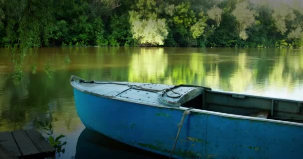 Oude blauwe boot vastgebonden met een touw aan houten pier zachtjes bobs op de stroom van de rivier — Stockvideo