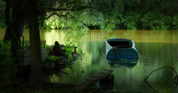 Oude blauwe boot vastgebonden met een touw aan houten pier zachtjes bobs op de stroom van de rivier — Stockvideo