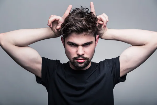 Young man in black T-shirt with fashionable hairstyle shows horns — Stock Photo, Image