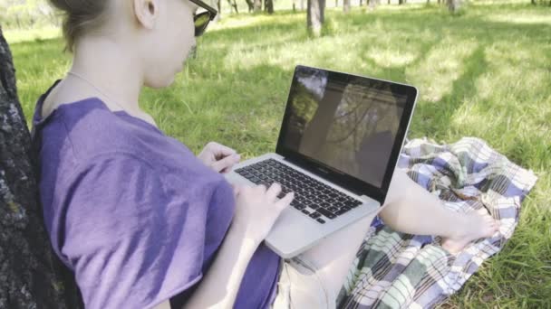 Kvinna i glas använder bärbar dator i parken. — Stockvideo