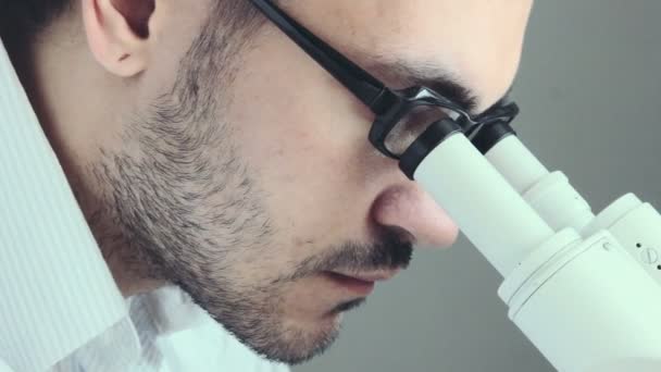 Молодой врач смотрит через микроскоп — стоковое видео