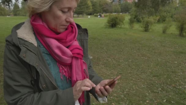 Vuxen kvinna med smartphone i parken — Stockvideo